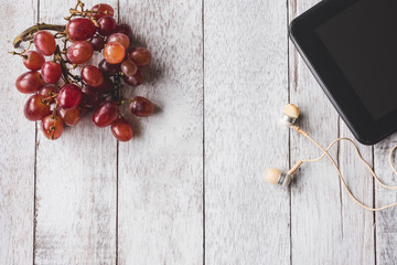 Top view of Red grapes with tablet and earphone on white wooden table