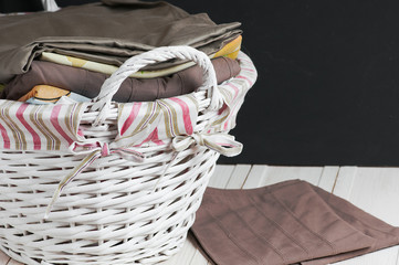 bedclothes of different colors in wicker basket on light background