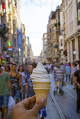 Hand holding vanilla ice cream, people in the street.