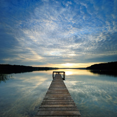 Fototapeta na wymiar Long Wooden Pier into a Calm Lake at Sunrise