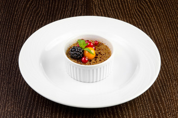 Creme brulee with red currants, blackberries, mint and winter cherry on a dark wooden background