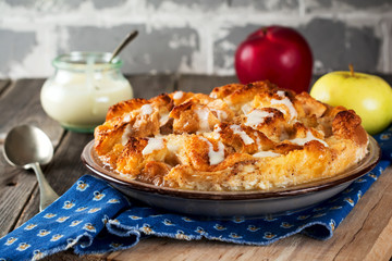 Bread pudding breakfast casserole with apples and vanilla sauce on the old wooden background. Selective focus.