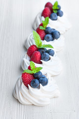 Mini  Pavlova meringue cakes with berries and mint on white wood
