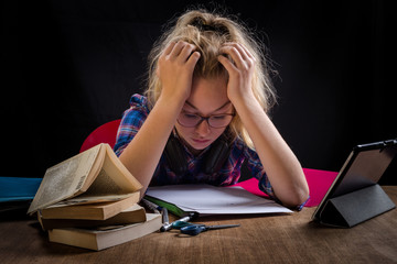 une adolescente , la tête dans les mains, est en difficulté devant ses devoirs scolaires