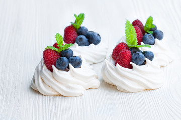 Mini  Pavlova meringue cakes with berries and mint on white wood