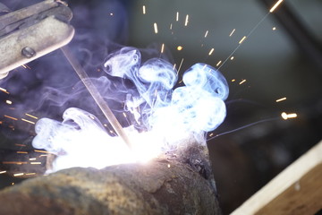 Fototapeta na wymiar Iron welding with bright light and smoke at manufacturing