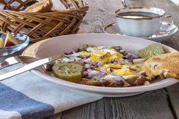 Scrambled eggs with bacon and pickles,toasted bread, butter,  pieces of apple, coffee, for breakfast.