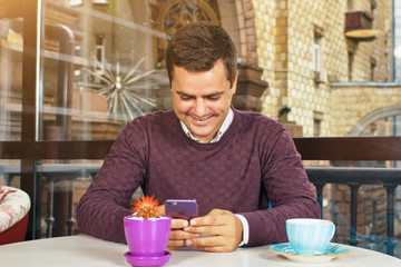 Fototapeta na wymiar Young man holding a mobile phone and smiling. Read the posts and drinking coffee.