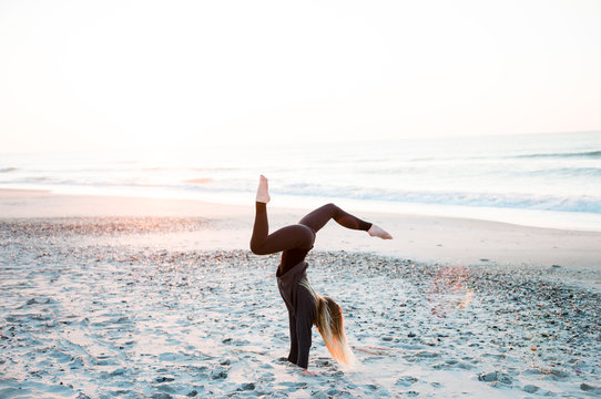 Woman Doing Handstand Yoga On Beach At Sunrise