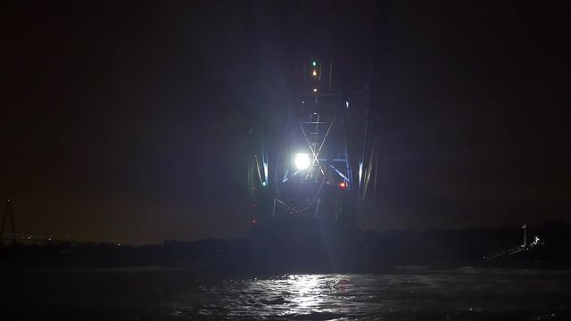 Shrimping trawler sails out to sea at night to fish.