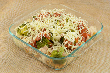 Casserole preparation with pasta, canned chicken chunks and steamed broccoli with marinara sauce and shredded cheese.