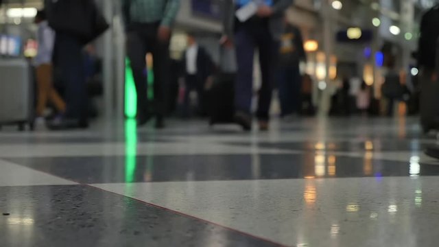 A low angle super slow motion shot of passengers walking in an airport terminal. Shallow depth of field.  	