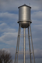 Tall silver water tower with cloudy blue sky background