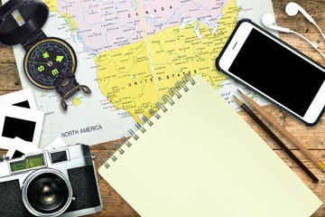 View from above of travel background. Retro camera,film slide,compass,smart phone, earphone,notebook,pencils and North America map on wooden table background. Elements of this image furnished by NASA
