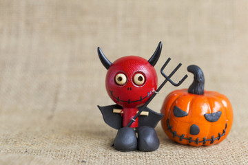 Halloween concept background, smiling red devil with halloween pumpkin on hessian background