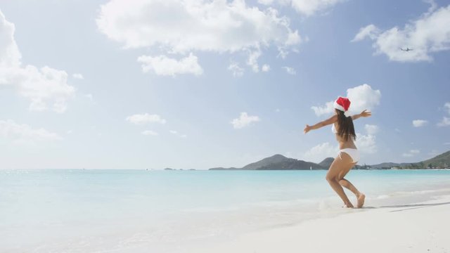 Christmas beach girl in santa hat jumping running having fun joyful and cheerful. Funny woman on Christmas vacation holidays travel getaway on white sand Caribbean beach. RED EPIC SLOW MOTION.