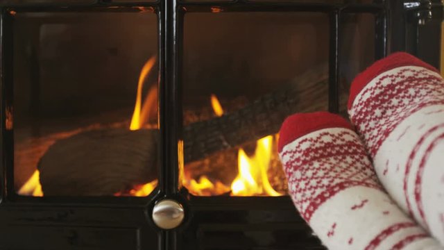 Feet in warm socks in front of fireplace in winter. Woman wearing socks against fireplace in living room. Female is warming her legs during winter. SLOW MOTION shot on RED EPIC.
