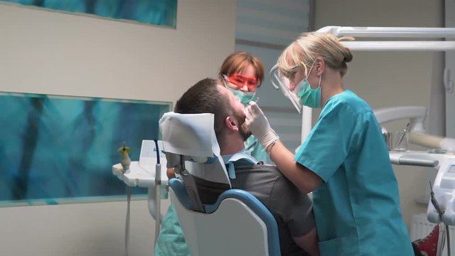Female dentist fills the tooth.Visit is in proffessional dental clinic. He is sitting on dental chair. He is young and has beard. Steadicam shot.
