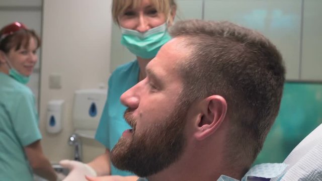 Female Dentist Preparing And Talking With Patient. Visit Is In Proffessional Dental Clinic. He Is Sitting On Dental Chair. He Is Young And Has Beard. Steadicam Shot.
