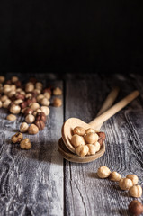 due cucchiai di legno sono pieni di nocciole tostate. Altre nocciole sono sparse su base di legno. Fotografia verticale