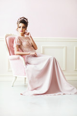 Beautiful young girl in a pink dress, sit in armchair