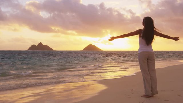 Enjoyment - free happy woman enjoying sunset. Serene woman in white embracing the golden sunshine glow of sunset with arms outspread and raised in sky enjoying peace, serenity on Lanikai, Oahu, Hawaii