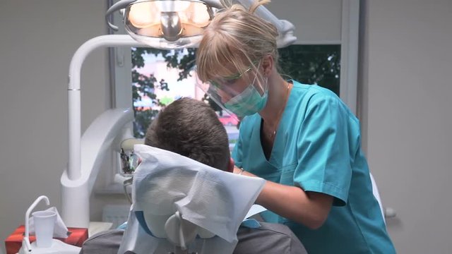 Female dentist at work in dental clinic. Visit is in proffessional dental clinic. He is sitting on dental chair. He is young and has beard. Steadicam shot.
