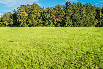 Roter Quadrokopter im Flug über grüner Wiese