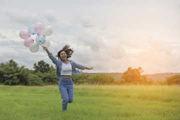 A beautiful young woman holding balloons , running along the pas