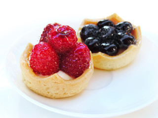 Delicious fruit cakes on a white plate. Sweet baked goods with raspberry and blueberry fruits.