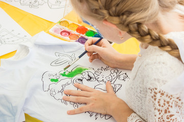 little blond girl paints a t-shirt with a brush