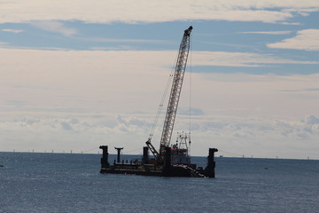 Cable laying rig with offshore wind turbine foundations rising out of the sea on the horizon for a...