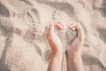 Hands of woman kids holding sandy to heart shape