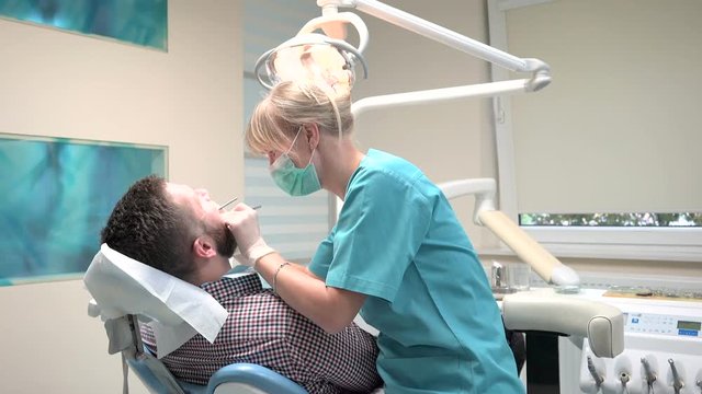 Dentist examining patient's teeth, explains him procedure. Male patient on visit at young female dentist. Visit is in proffessional dental clinic. He is sitting on dental chair.