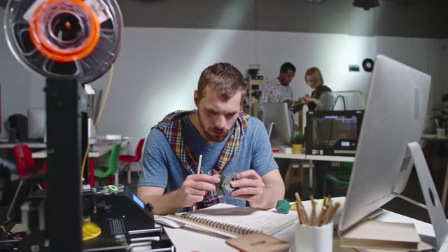 Panning shot of stylish engineer with beard sitting behind desk and testing puzzle made with FDM 3d printer