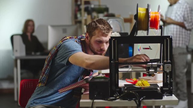 Lockdown of bearded engineer operating FDM 3d printing machine and looking at his notes