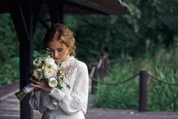 Fototapeta premium Bride stands in the garden holding a wedding bouquet behind her