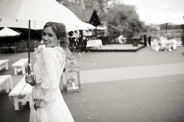 Bride smiles standing in the rain under an umbrella