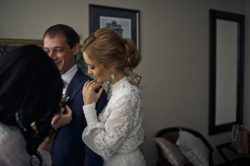 Bride leans to groom's shoulder while another woman adjusts a bo