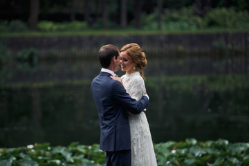 Fototapeta premium Smiling wedding couple stands in the dark wood behind a lake