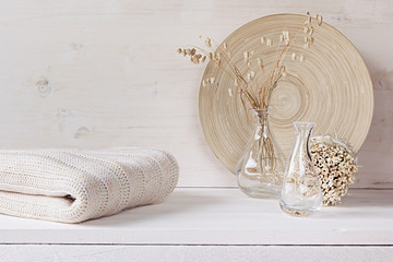 Soft home decor of  glass vase with spikelets and knitted fabric on white wood background. Interior.