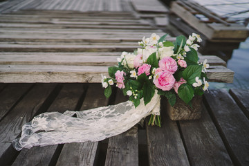 Beautiful bouquet of jasmine and pink garden roses with lace ribbons on old wooden pier