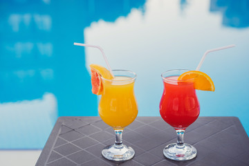 Fresh alcoholic cocktails near the swimming pool at resort. Red and orange longdrinks with ice garnished with fruits.