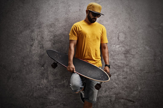 Skater holding longboard and leaning against wall