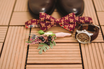 set of groom shoes, bow tie, watch and boutonniere lie on the background of wooden floor with stripes and texture