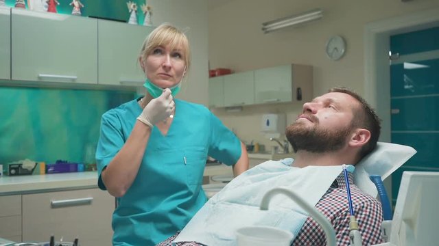 Female dentist examining an drilling patient's tooth. Visit is in proffessional dental clinic. He is sitting on dental chair. He is young and has beard. Dolly and steadicam shot.
