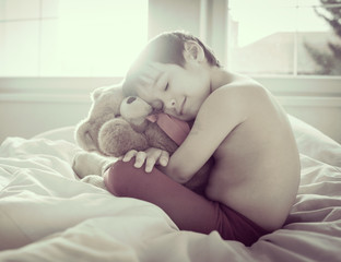 Fototapeta na wymiar A little cute boy with Teddy bear on the bed