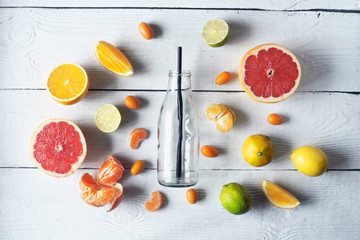 Glass bottle surrounded by different citrus on the white wooden table top view