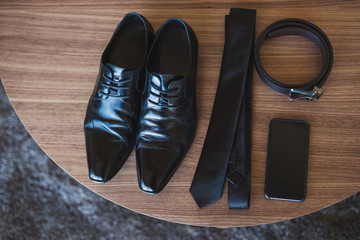 male black shoes, tie, belt and cell phone on wooden table