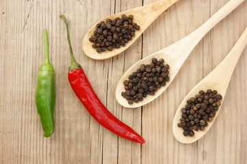 Black and red pepper in wooden spoon on the old board